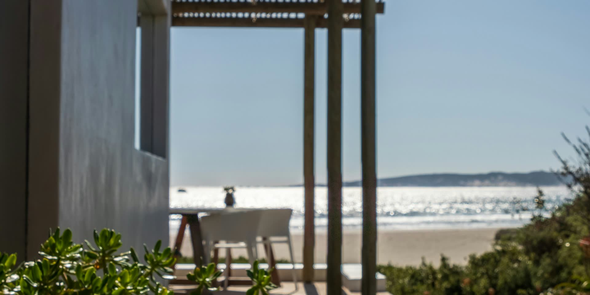 Sunlight sparkling on the Atlantic beyond a beachfront patio table
